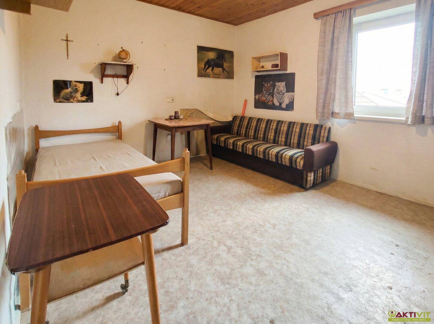 Schlafzimmer mit Einzelbett, Sofa, Holztisch und Holzdecke.