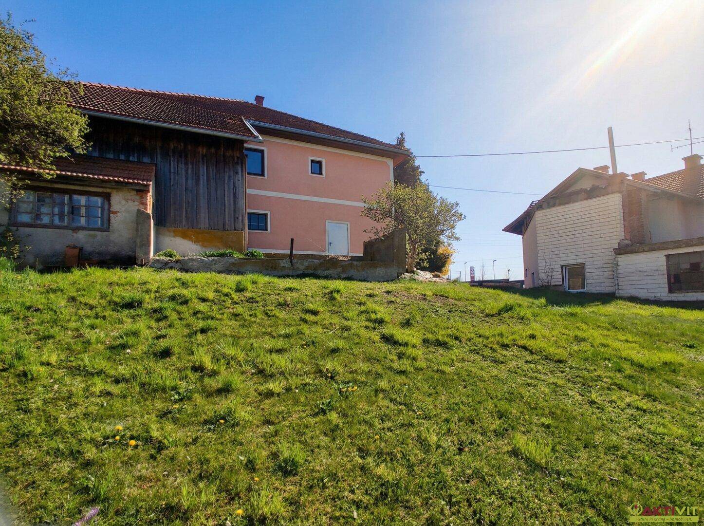 Wohnhaus und Scheune von einem grünen Hügel aus gesehen unter strahlendem Sonnenschein.