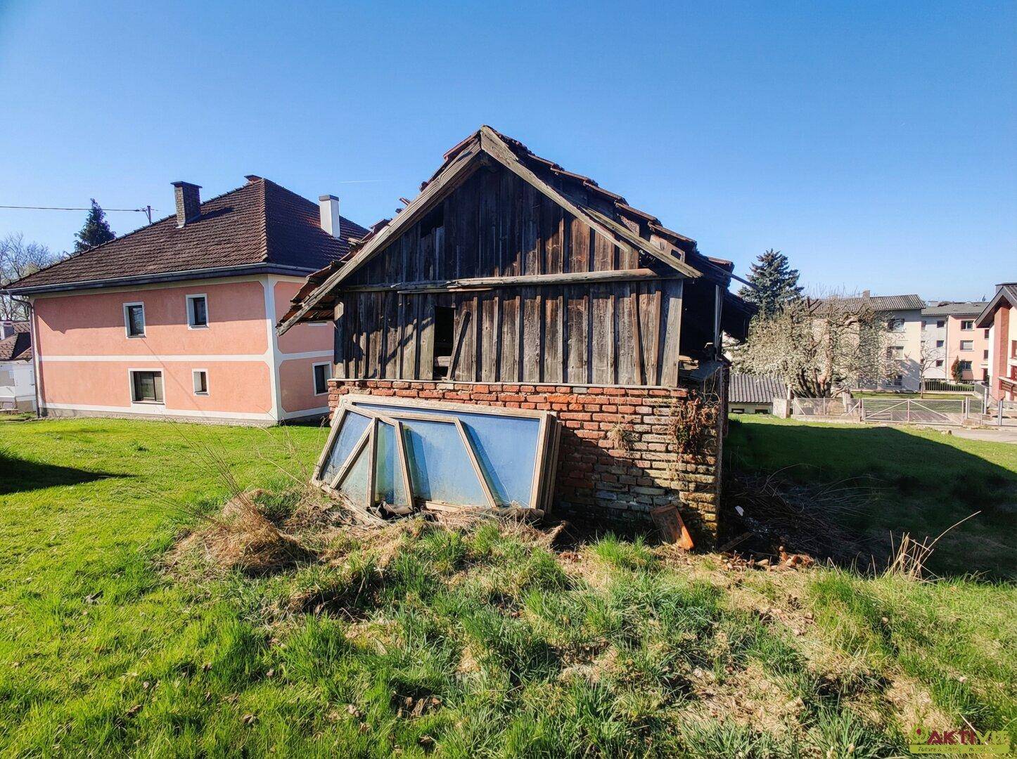 Alte Holzscheune mit Ziegelmauerwerk und abgestellten Fenstern im Freien.