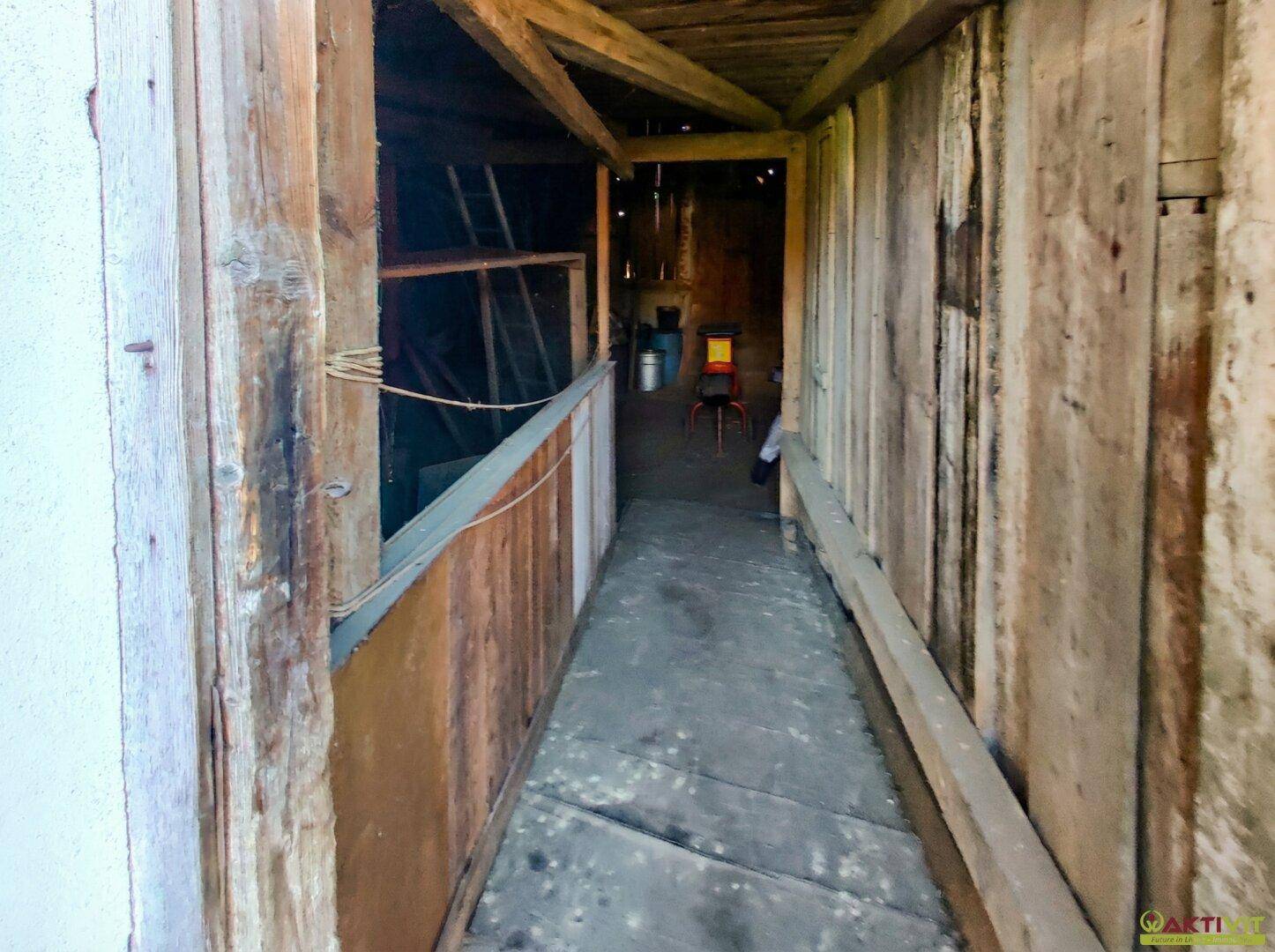 Innenansicht des Holzschuppens mit sichtbarer Holzkonstruktion und schmalem Gang.