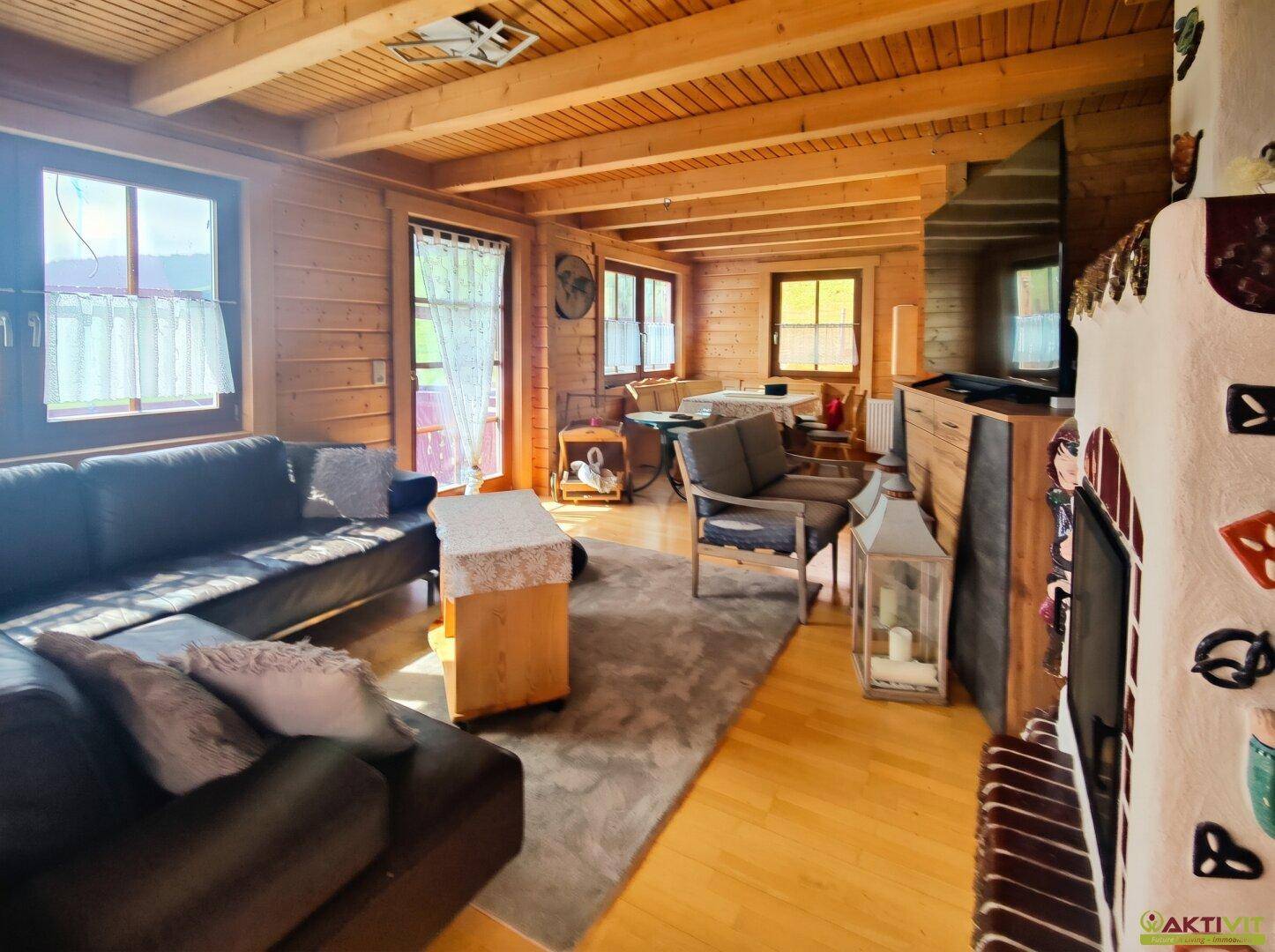 Gemütlicher Wohn- und Essbereich mit Holzbalkendecke, Kamin und Zugang zum Balkon.