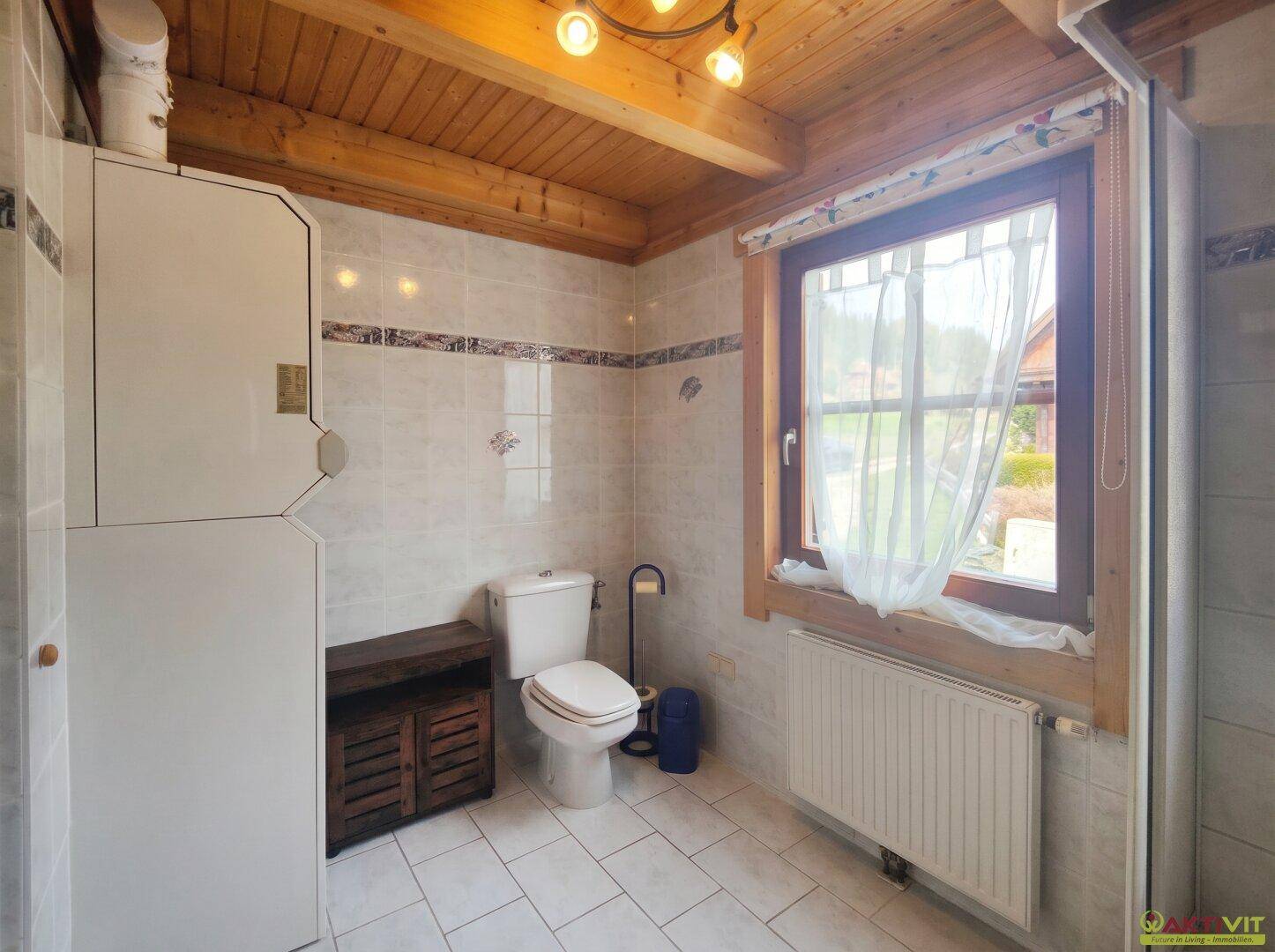 Badezimmer mit WC, Fliesenboden und Holzdecke, ausgestattet mit einem Fenster.