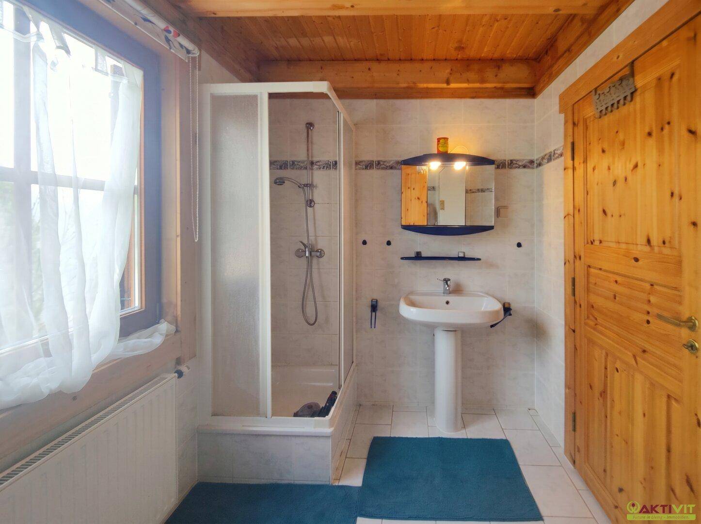 Helles Badezimmer mit Duschkabine, Waschbecken und Holzdecke.