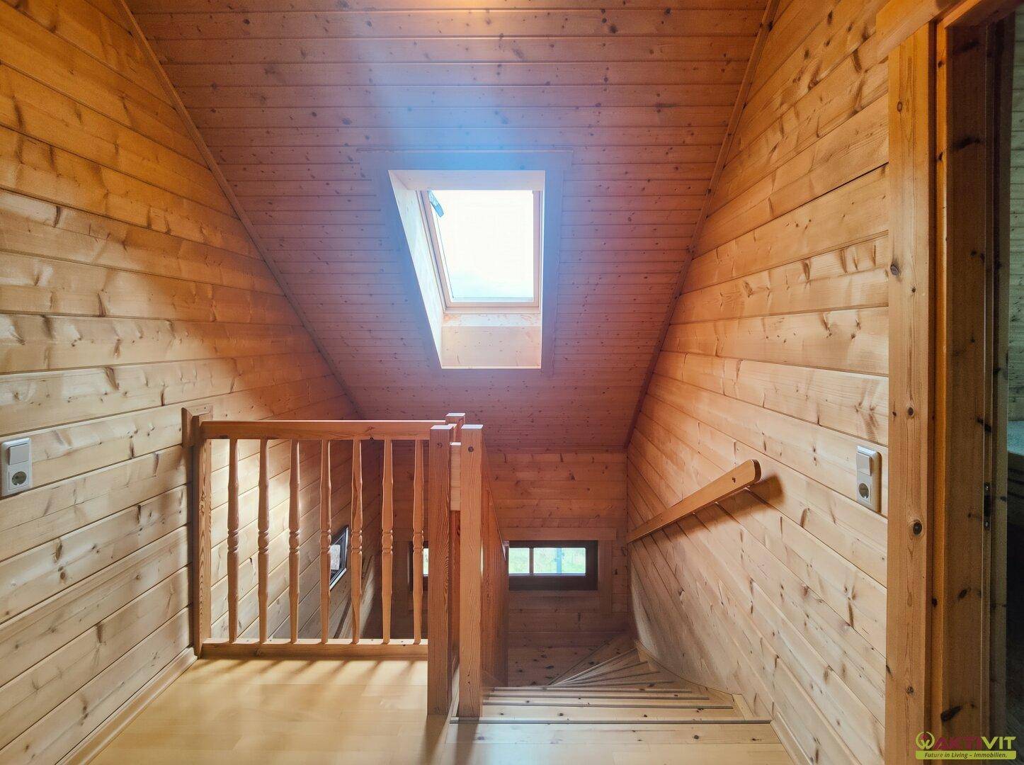 Holzvertäfelter Treppenaufgang mit Dachfenster, der die oberen Etagen verbindet.