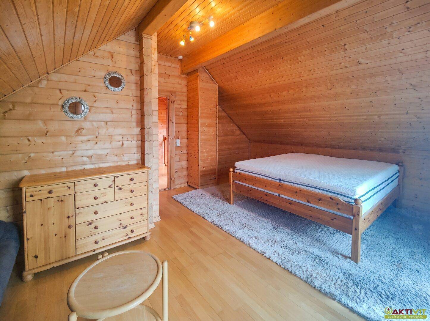 Gemütliches Schlafzimmer mit Holzwänden, Dachschräge und Doppelbett unter Dachfenster.