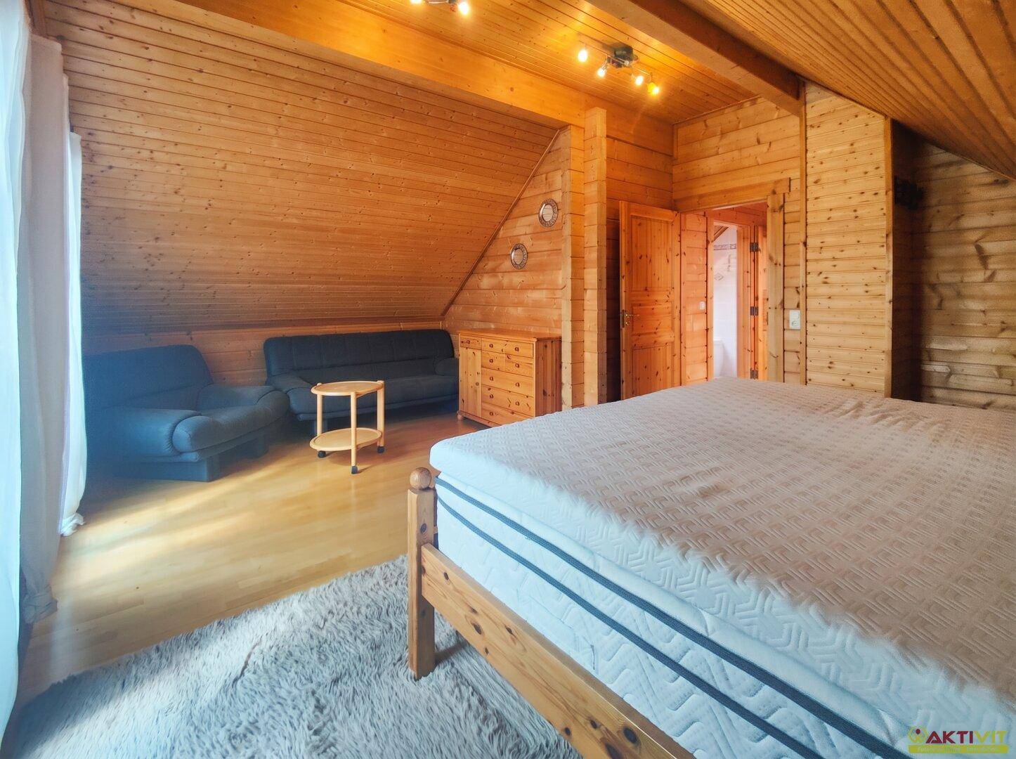 Geräumiges Schlafzimmer mit Holzwänden, Dachschräge und Sitzbereich.