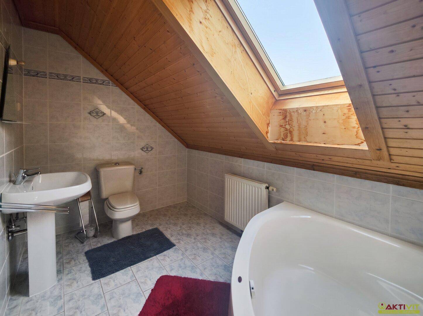 Badezimmer im Dachgeschoss mit Badewanne, Waschbecken und Dachfenster.