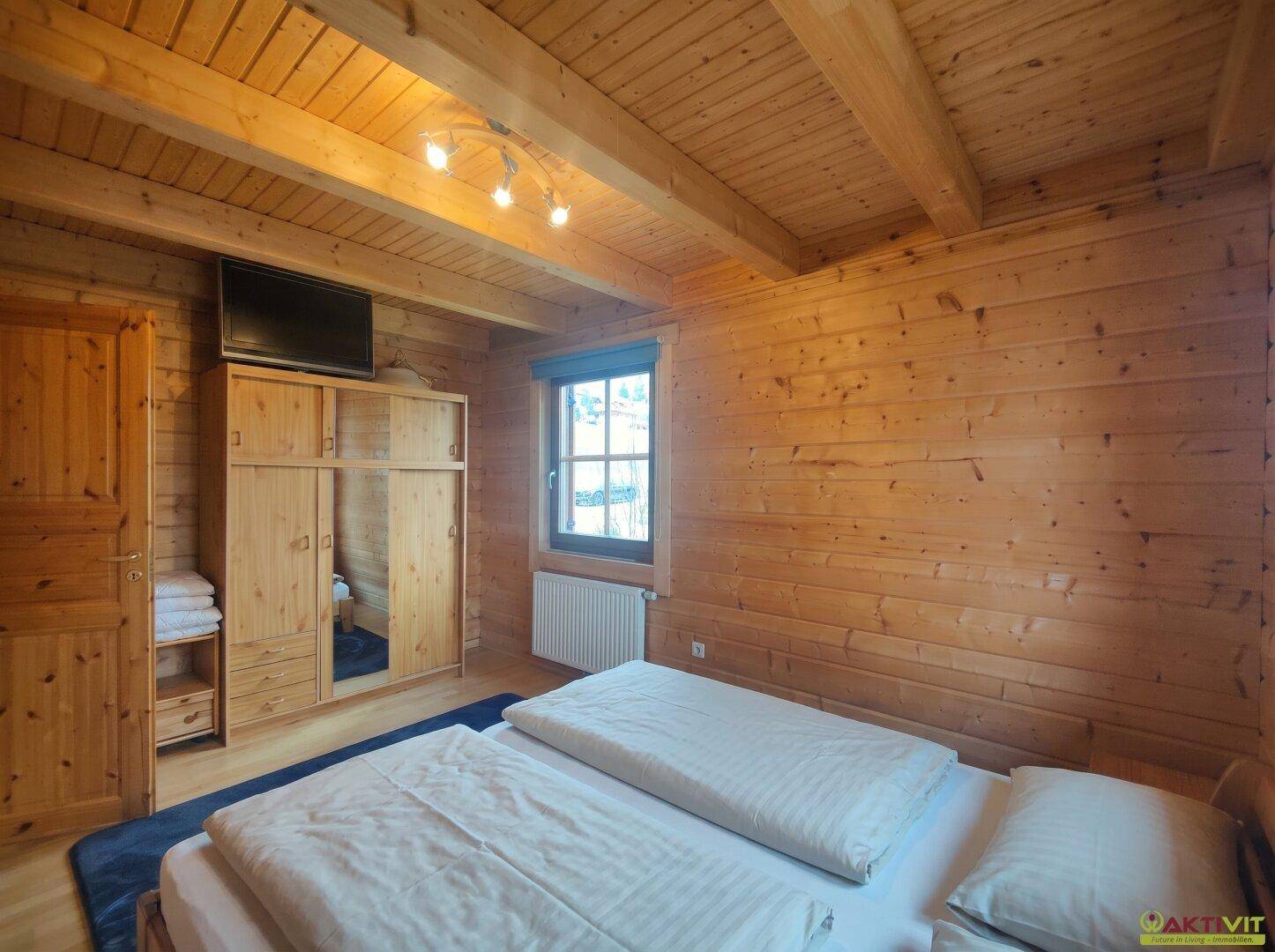 Schlafzimmer mit Holzwänden, Doppelbett und Kleiderschrank.
