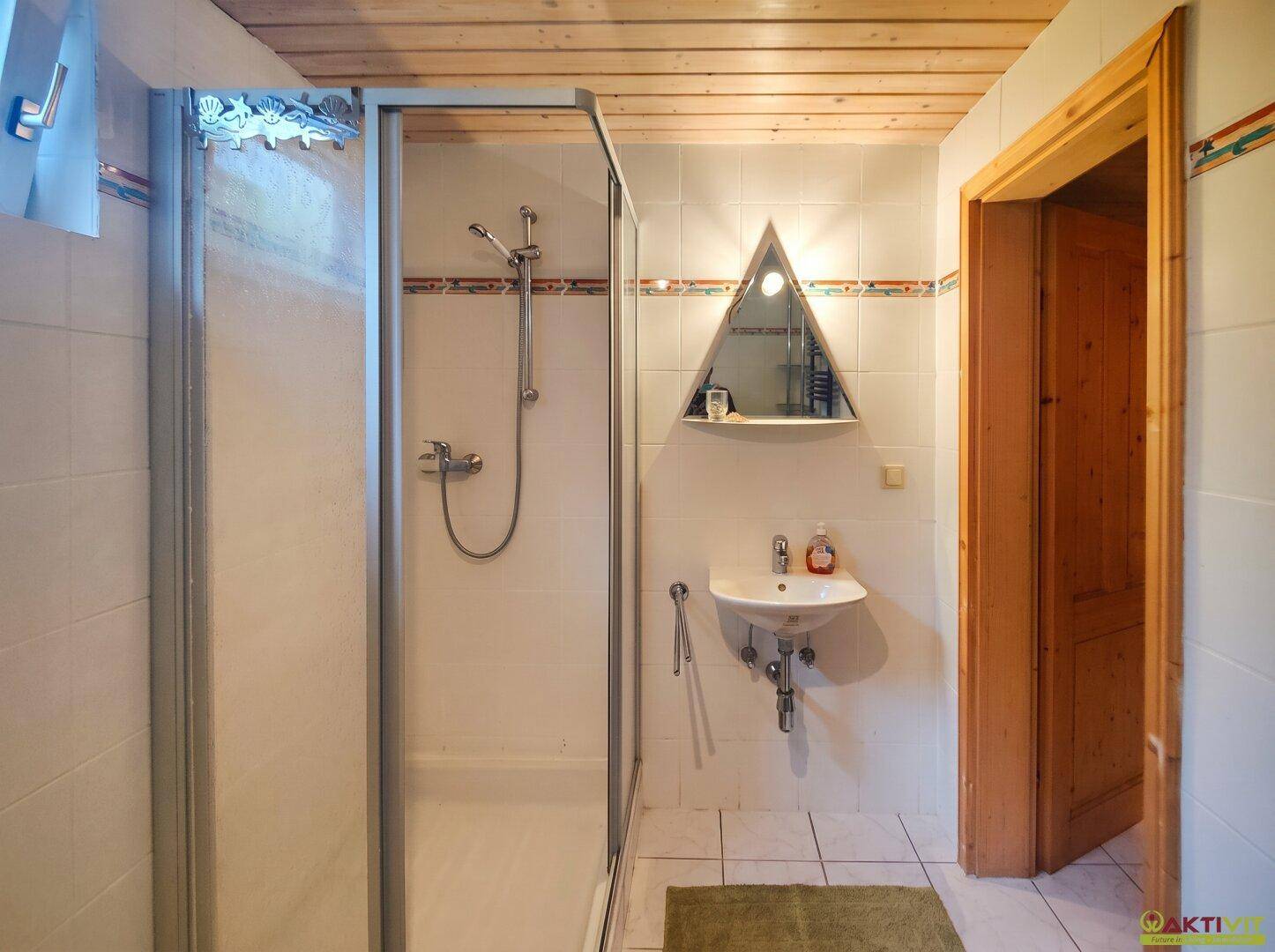 Kleines Badezimmer mit Duschkabine, Waschbecken und Fliesenboden.