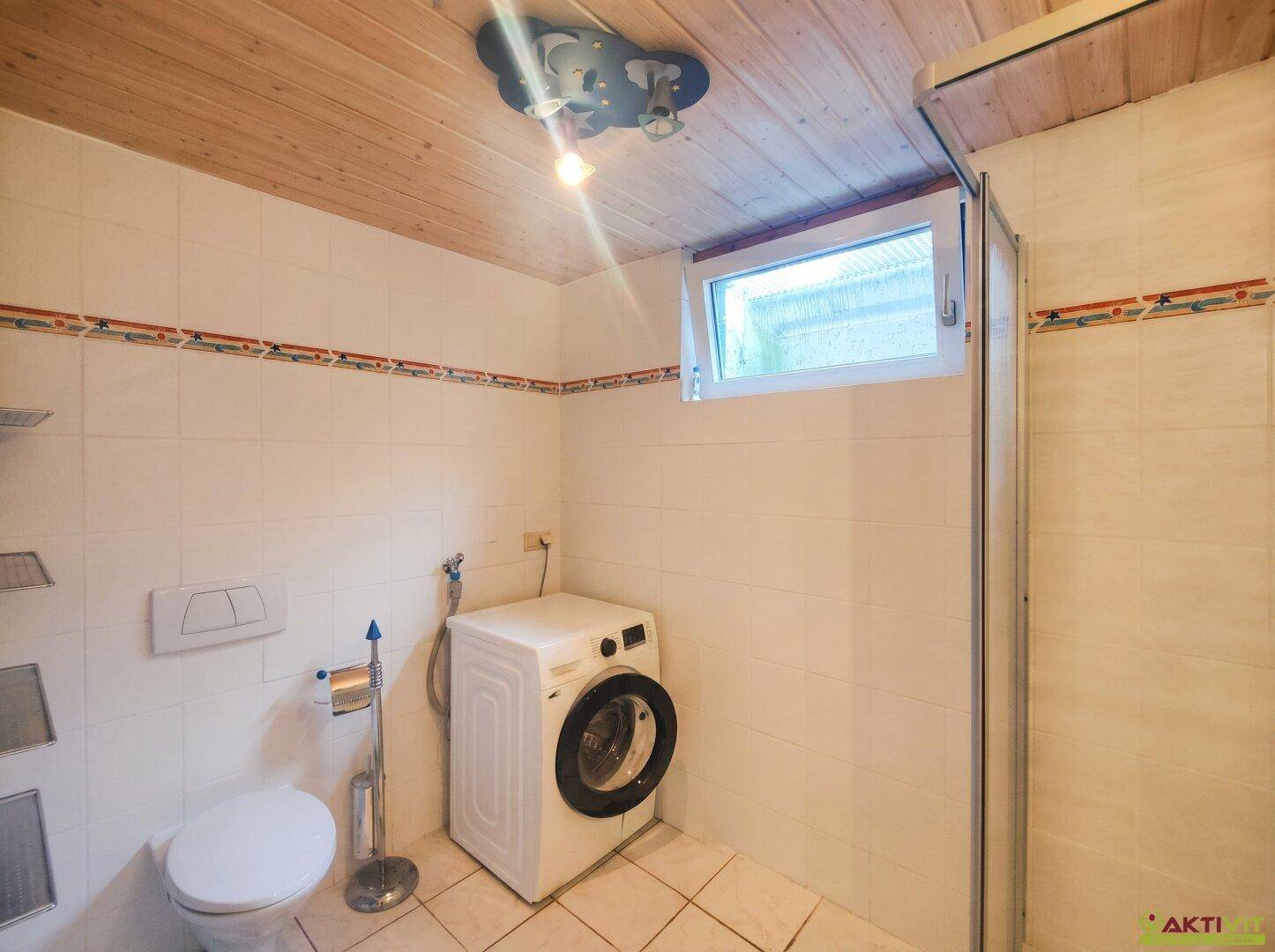 Hauswirtschaftsraum mit Waschmaschine, WC und Duschkabine.