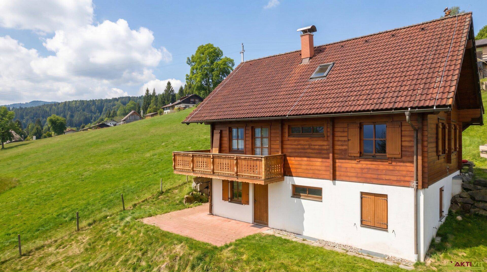 Traditionelles Holzhaus mit Terrasse und weitläufiger grüner Wiese unter blauem Himmel.