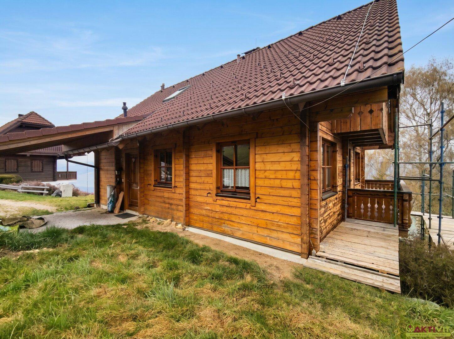 Seitenansicht des Holzhauses mit Holzbalkon und Zugang zum Carport.