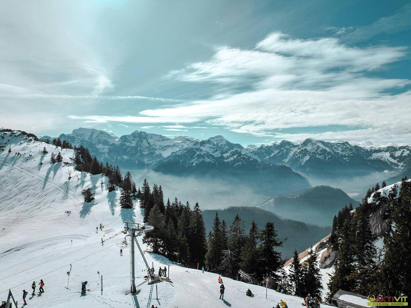 Weitläufige Winterlandschaft mit Skipiste, Lift und schneebedeckten Bergen in der Ferne.
