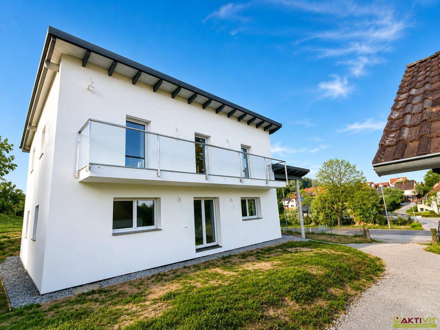 Modernes Einfamilienhaus mit weißer Fassade, Balkon und Blick auf die Umgebung.