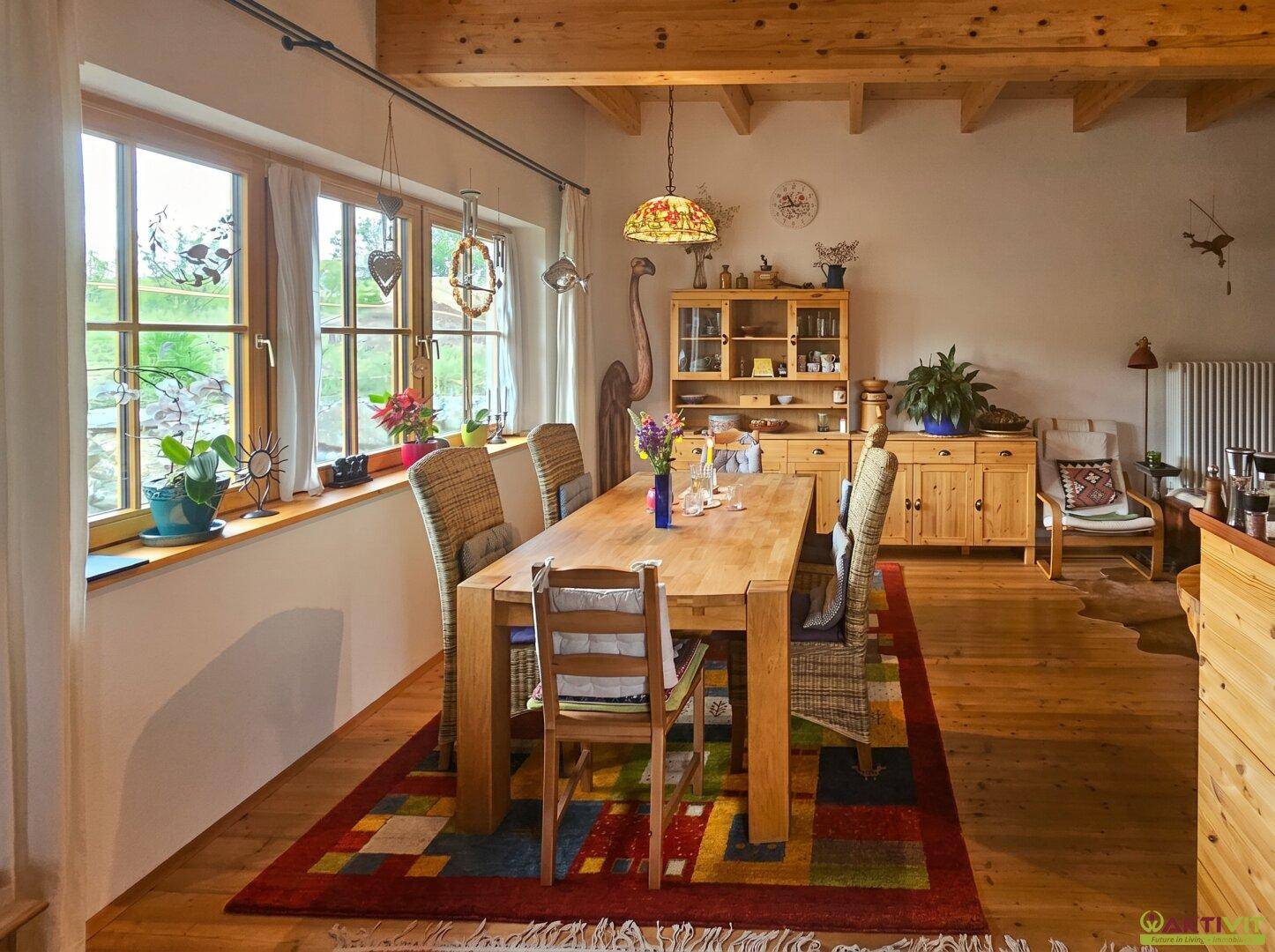 Heller Essbereich mit großem Holztisch, Korbstühlen und Fenstern mit Blick in den Garten.
