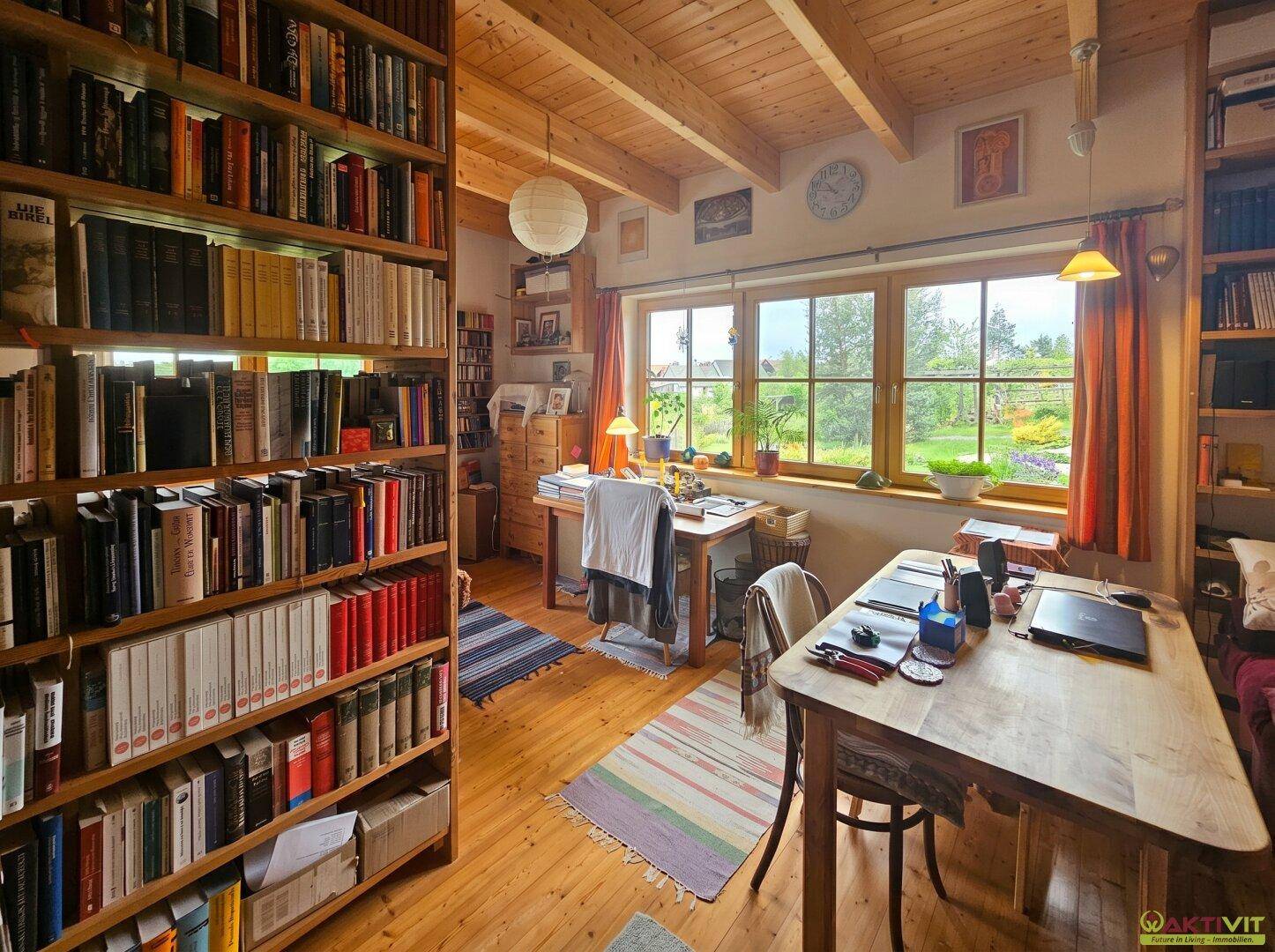 Helles Arbeitszimmer mit Holzbalkendecke, Bücherregalen und zwei Schreibtischen mit Gartenblick.