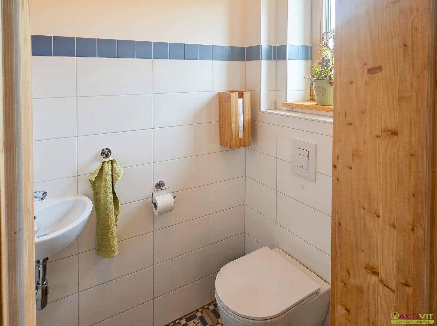 Kleines Gäste-WC mit Fenster, Wand-WC und Handwaschbecken in schlichtem, funktionalem Design.