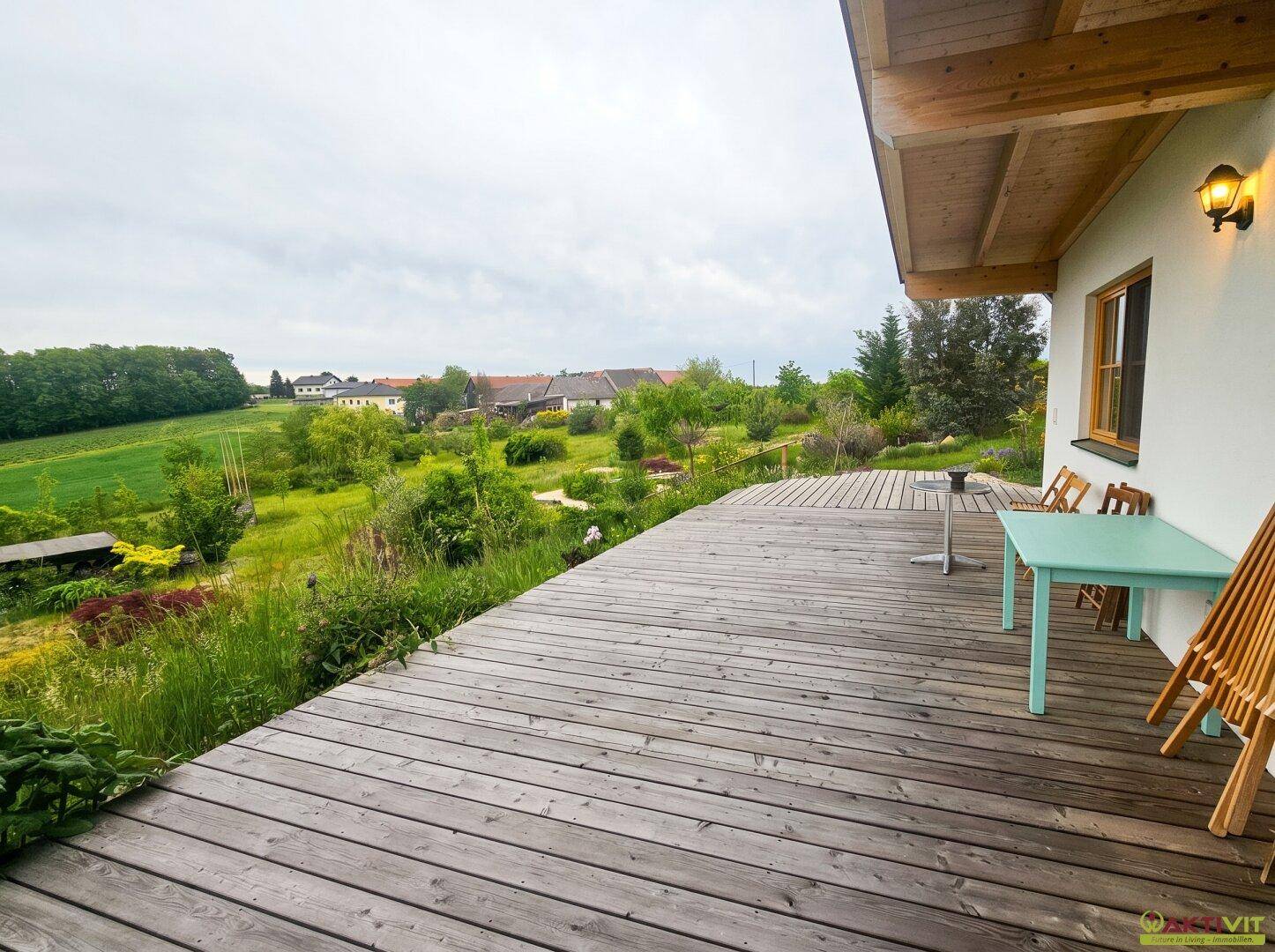 Weitläufige Holzterrasse am Haus mit Sitzgelegenheiten und Panoramablick ins Grüne.