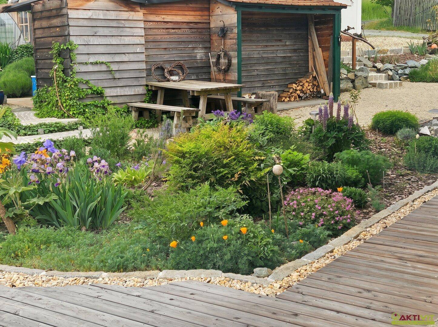Blühender Gartenbereich mit Gartenhaus, Picknicktisch und vielfältiger Bepflanzung.