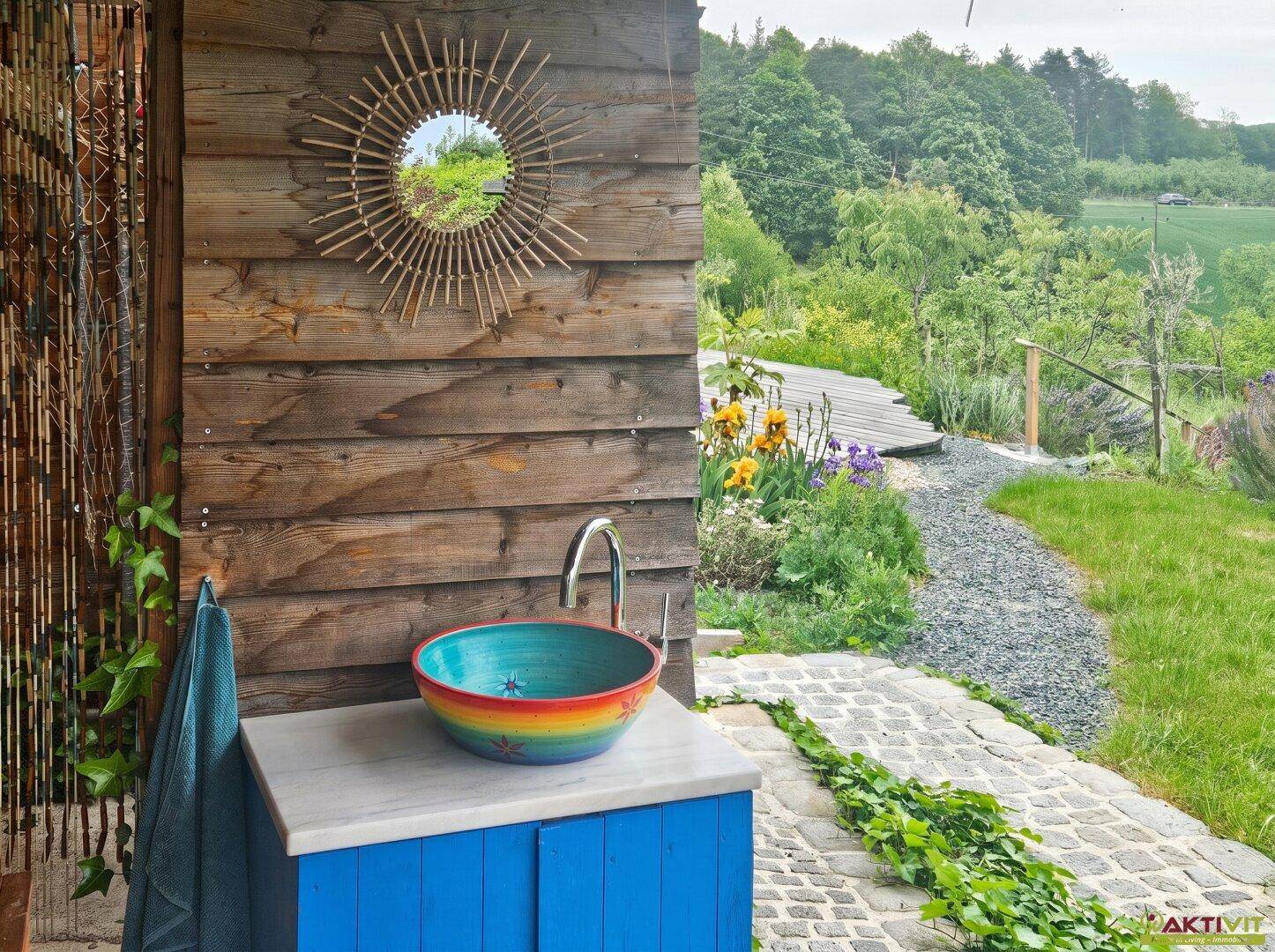 Origineller Außenwaschplatz mit farbenfrohem Waschbecken und Blick in den naturnahen Garten.