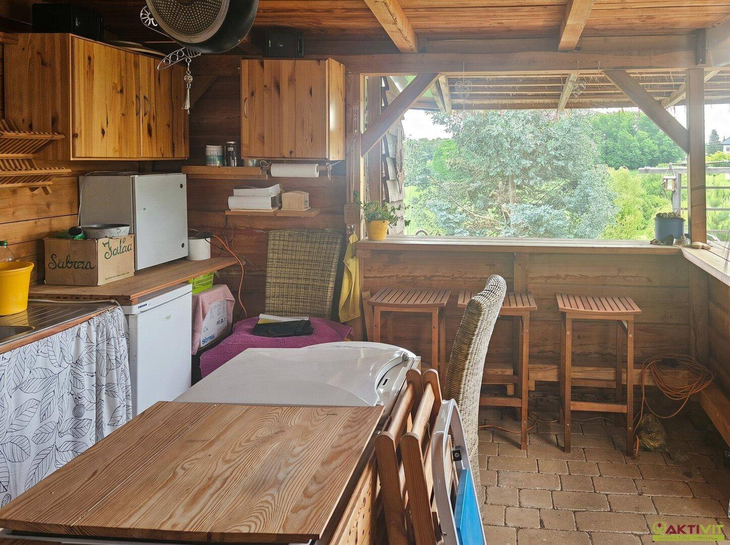 Gemütlicher Essbereich in der rustikalen Außenküche mit Blick in die Natur.