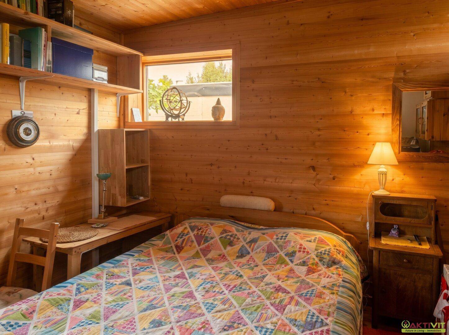 Schlafzimmer mit Holzwänden und -decke, gemütlichem Bett und kleinem Fenster.
