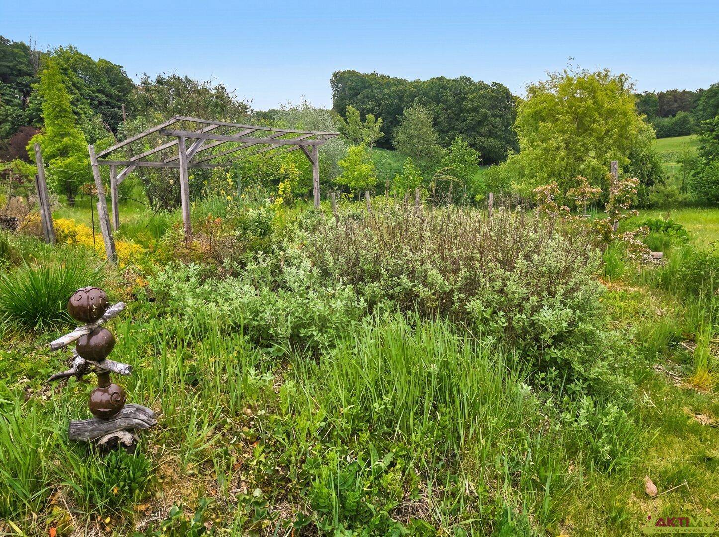 Naturnaher Gartenbereich mit vielfältiger Bepflanzung und einer Holzpergola.