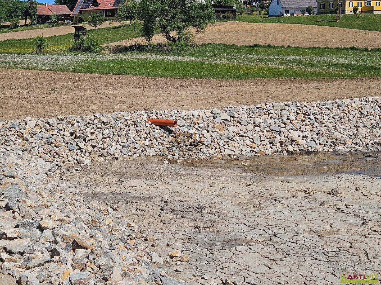 Detailansicht einer Steinmauer und trockener Erde mit einem Abflussrohr in einer ländlichen Landschaft.