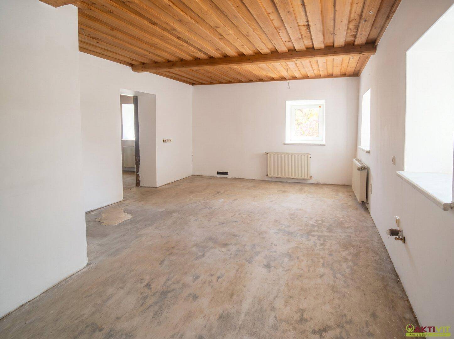 Leerer Raum mit Holzbalkendecke, weißen Wänden und Betonboden, bereit für die Gestaltung.