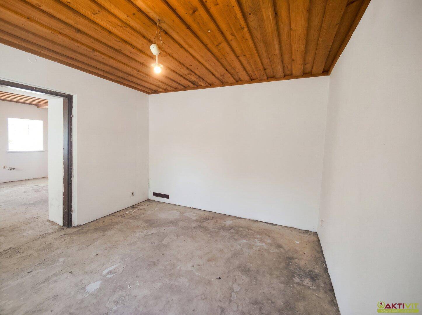Unmöblierter Raum mit Holzbalkendecke, weißen Wänden und Betonboden, ideal für individuelle Nutzung.