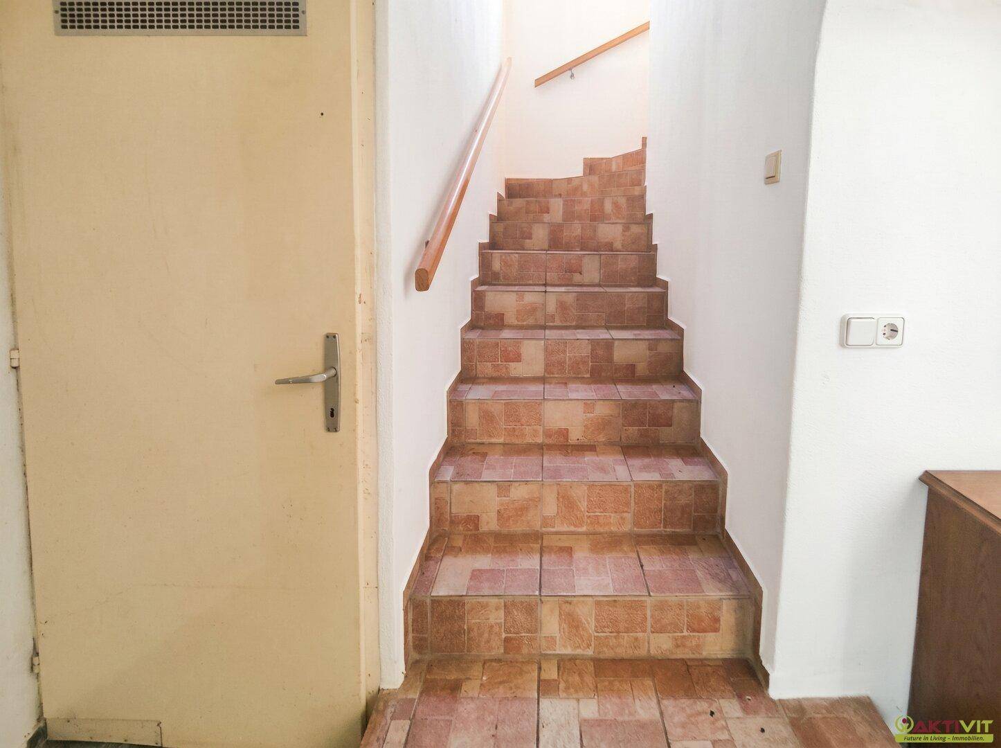 Geflieste Treppe mit Holzgeländer, die in die oberen Stockwerke des Hauses führt.