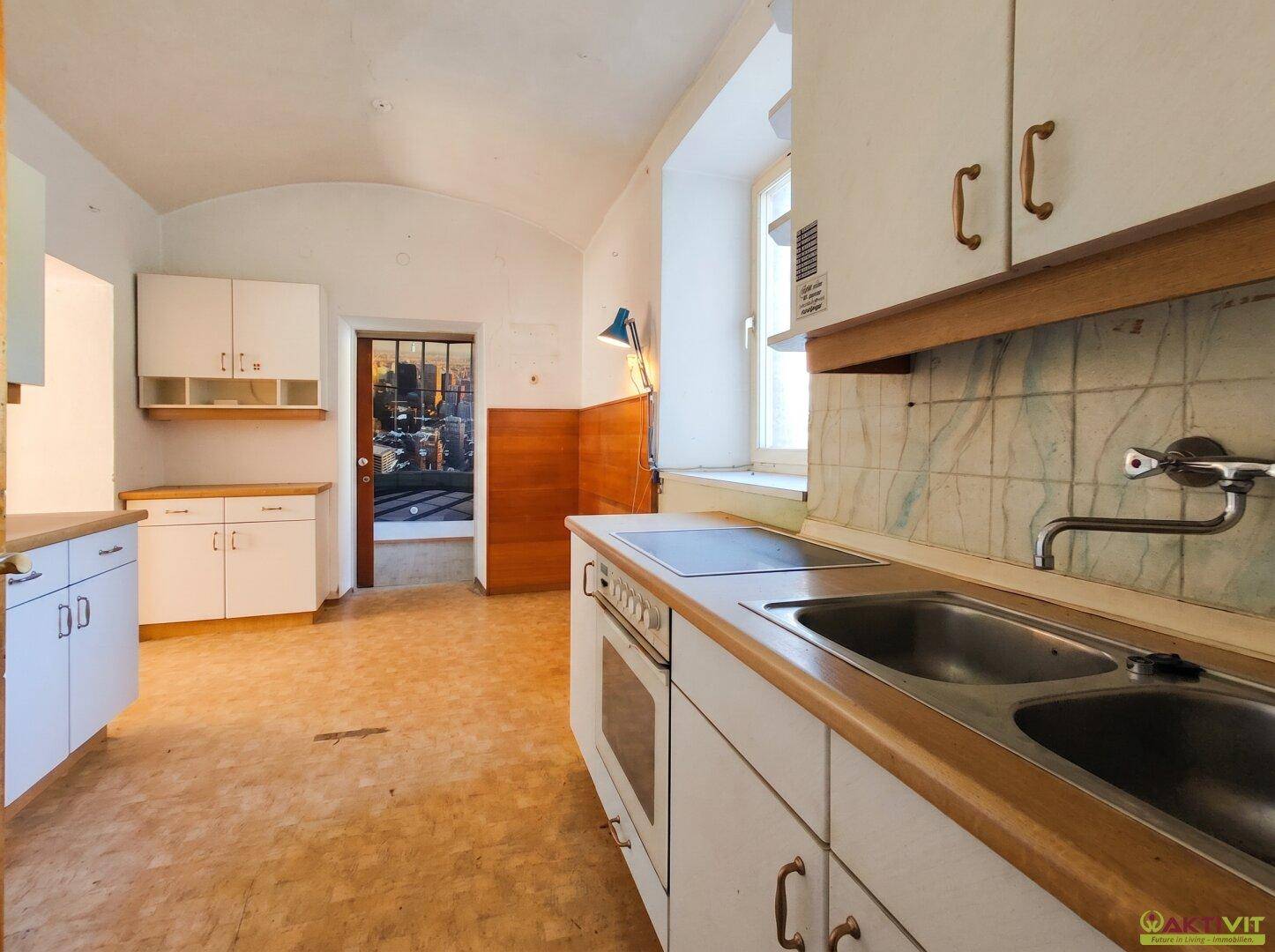 Küchenbereich mit Doppelspüle, Kochfeld, gefliestem Spritzschutz und weißen Schränken.