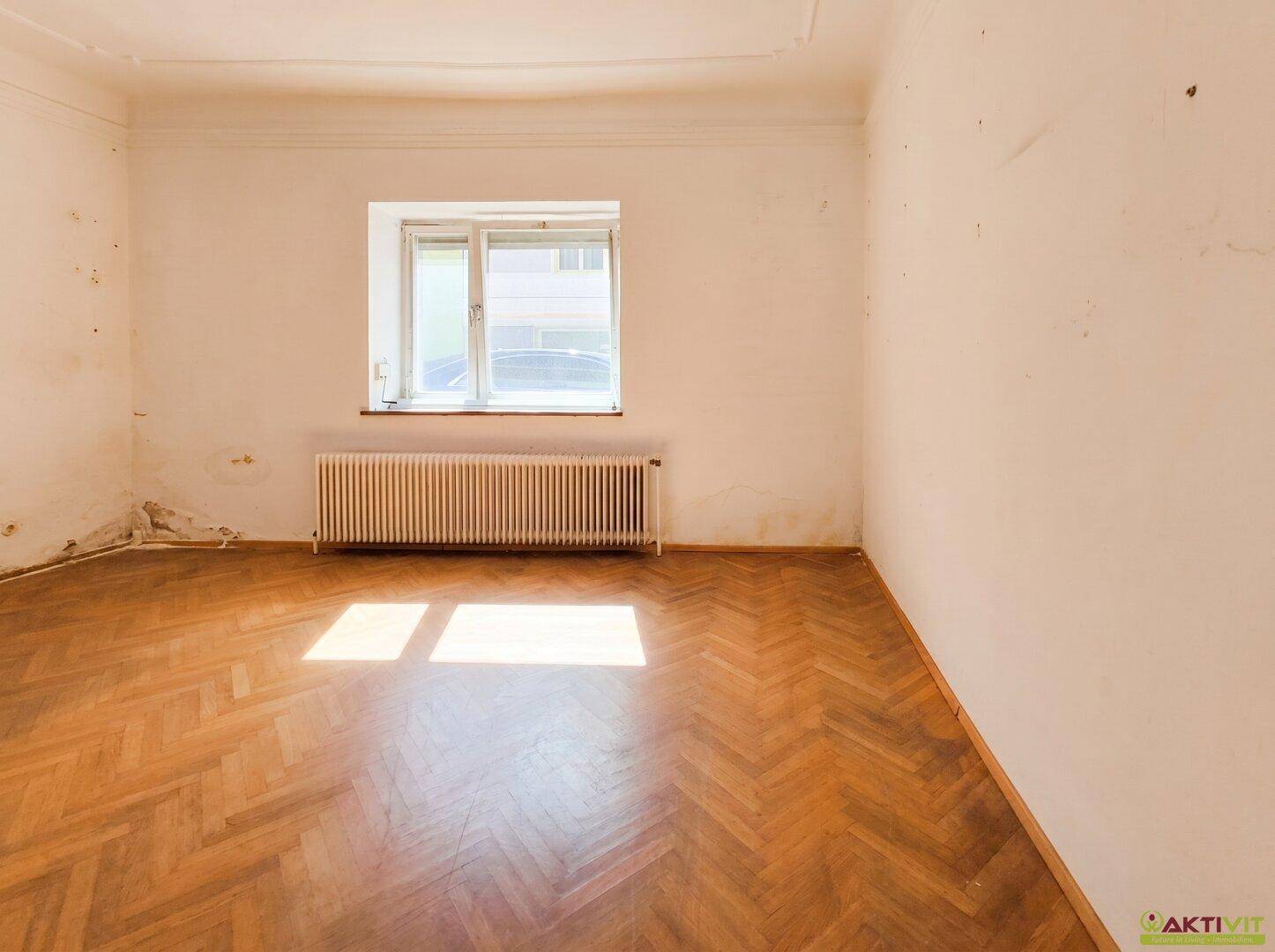 Helles Schlafzimmer mit Fischgrätparkett, einem Fenster und Heizkörper.