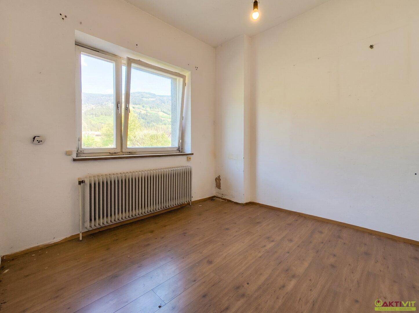 Schlafzimmer mit Laminatboden, großem Fenster und weitem Blick ins Grüne.