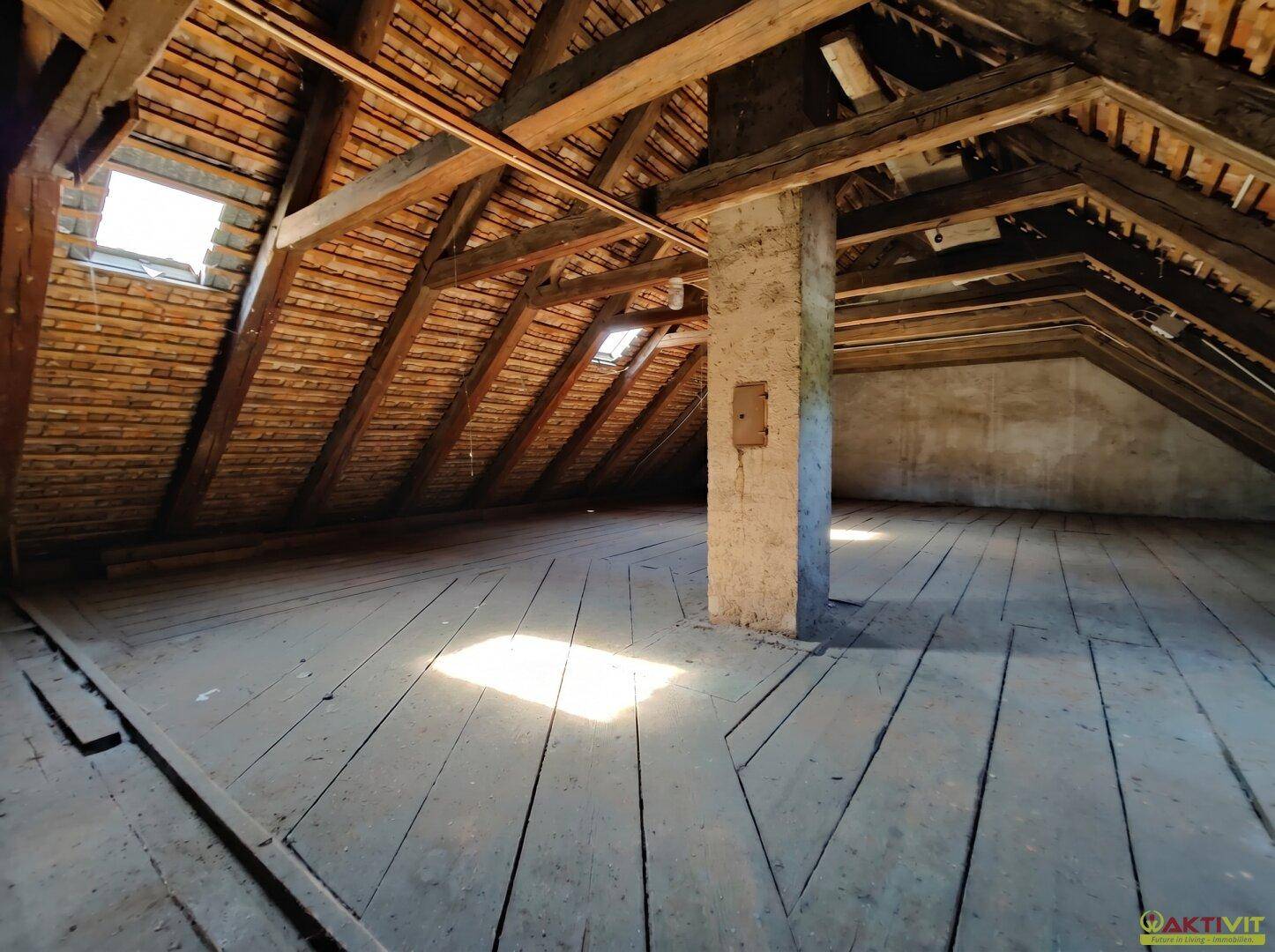 Unausgebauter Dachboden mit sichtbaren Holzbalken und Dachfenstern.