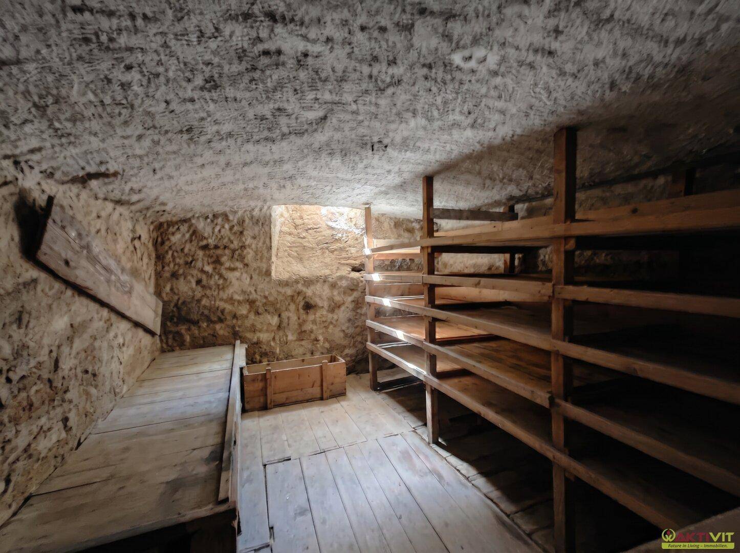 Kellerraum mit rauen Steinwänden und einfachen Holzregalen zur Lagerung.