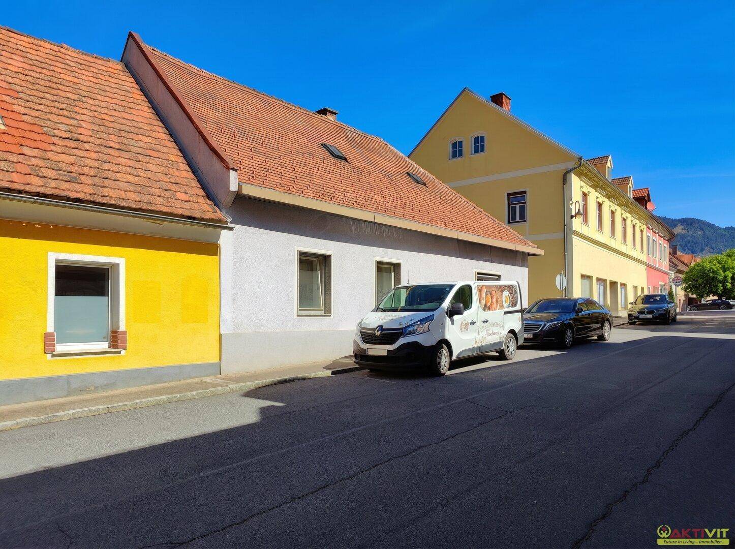 Straßenansicht des Gebäudes mit angrenzenden Häusern und parkenden Fahrzeugen.
