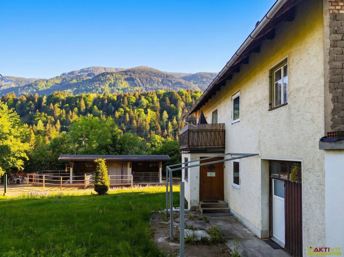 Seitenansicht des Hauses mit Balkon und weitem Blick auf die bewaldeten Berge.