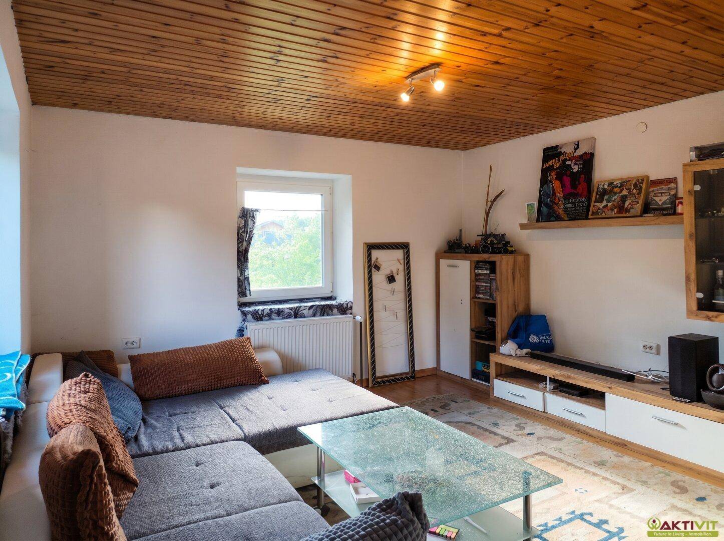 Gemütliches Wohnzimmer mit Holzbalkendecke, Sofa und Blick ins Grüne.
