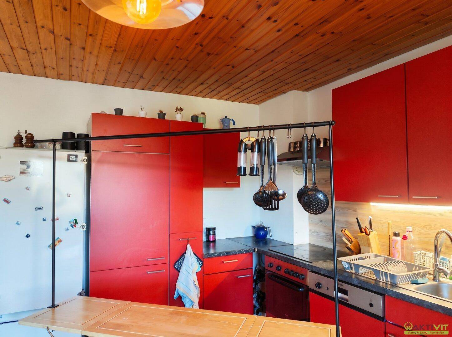 Küche mit roten Schränken, integrierten Geräten und Holzdecke.