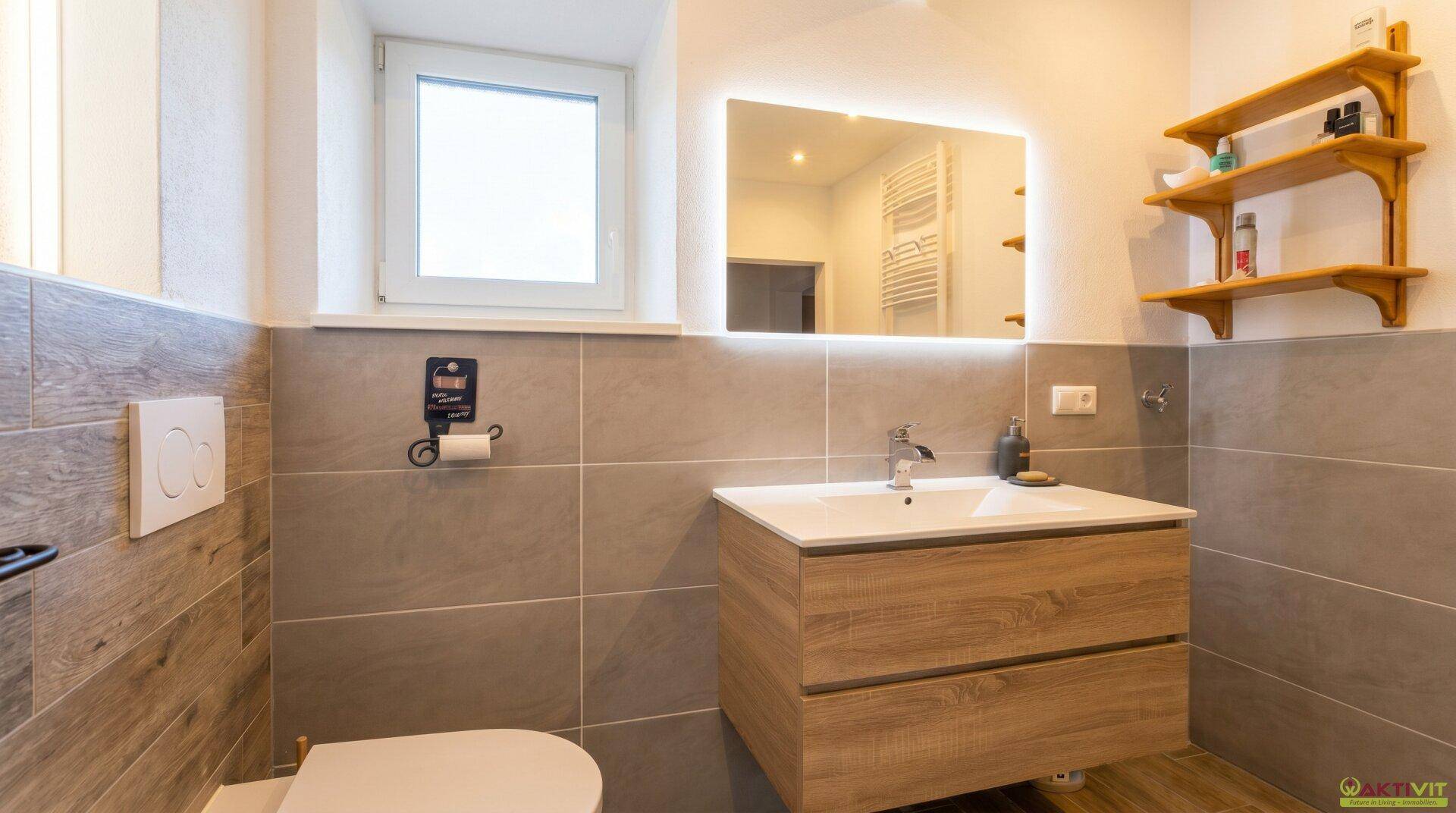 Modernes Badezimmer mit Waschtisch, beleuchtetem Spiegel und Wand-WC.