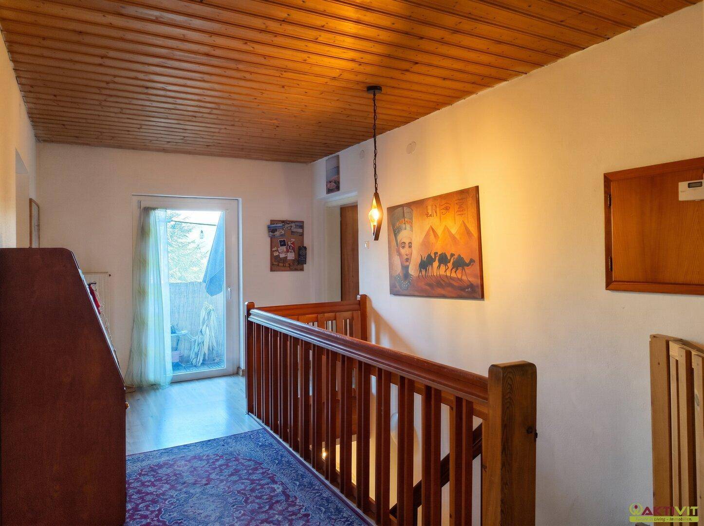 Heller Flur im Obergeschoss mit Holzgeländer, Teppich und Zugang zum Balkon.