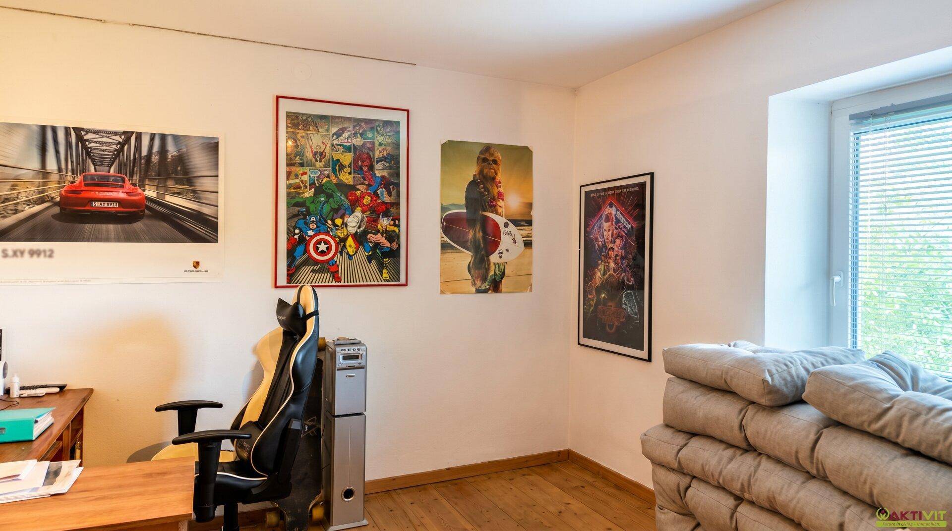 Helles Zimmer mit Holzboden, Fenster und verschiedenen Postern an den Wänden.