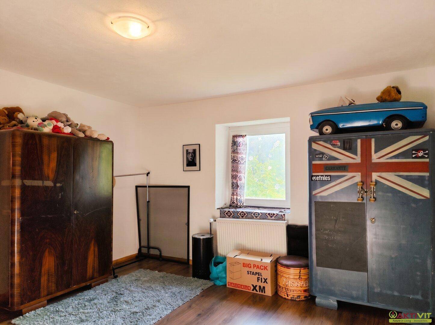 Schlafzimmer mit Holzboden, Fenster und zwei antiken Kleiderschränken.