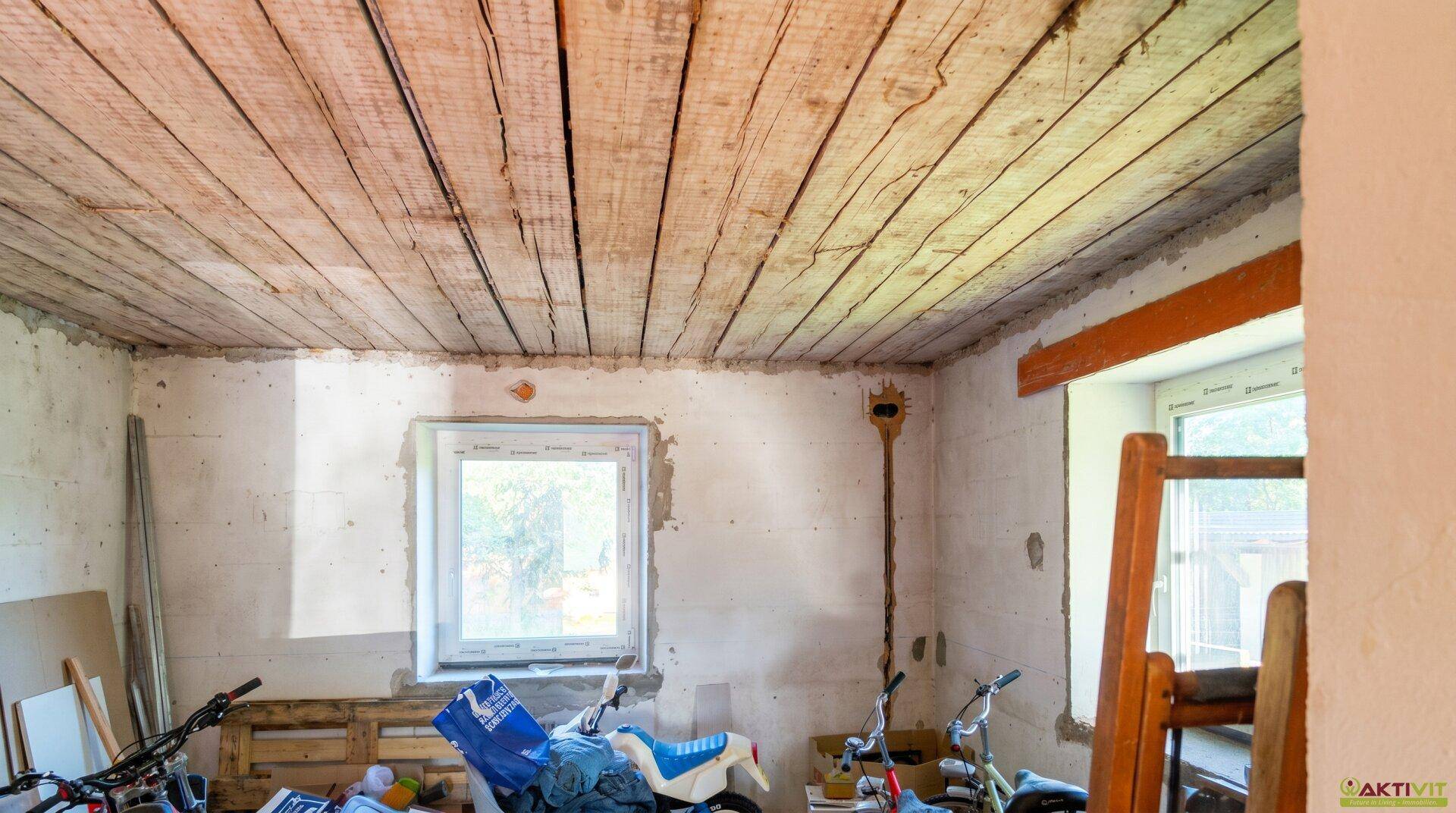 Renovierungsbedürftiger Raum mit Holzdecke und Fenster.