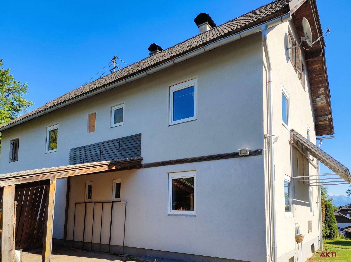 Seitenansicht des Hauses mit Fenstern, Balkon und Carport unter blauem Himmel.