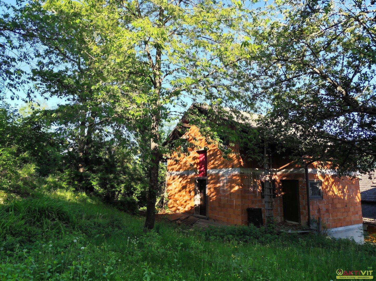 Rohbau eines Nebengebäudes oder Hauses umgeben von Bäumen und Grün.
