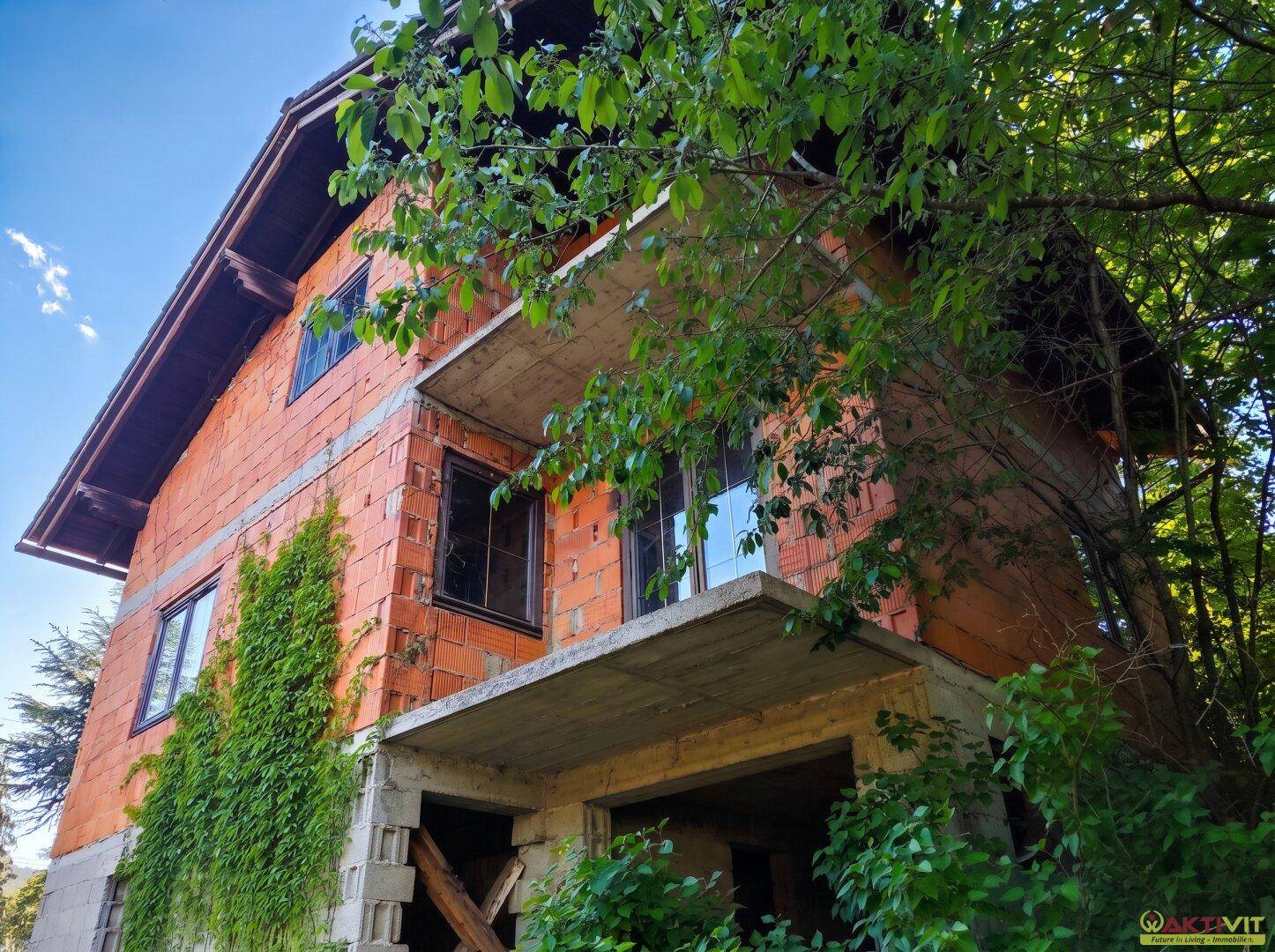 Rohbau eines Hauses mit Ziegelwänden und Betonbalkonen, umgeben von Vegetation.