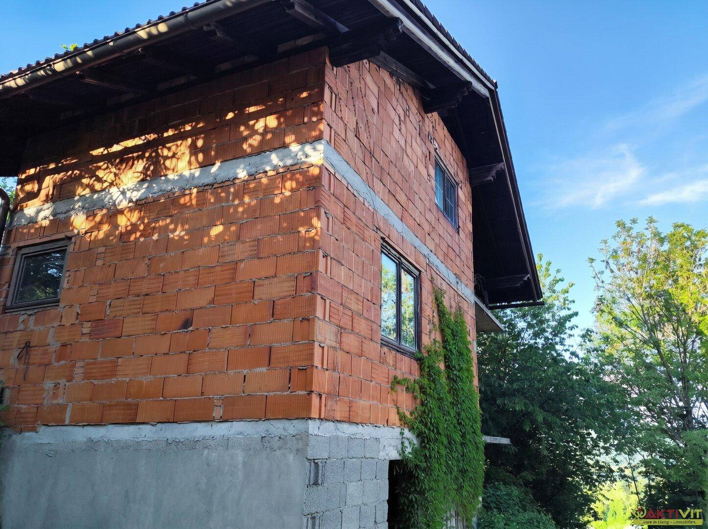 Seitenansicht des Rohbaus mit Ziegelwänden und grüner Kletterpflanze.