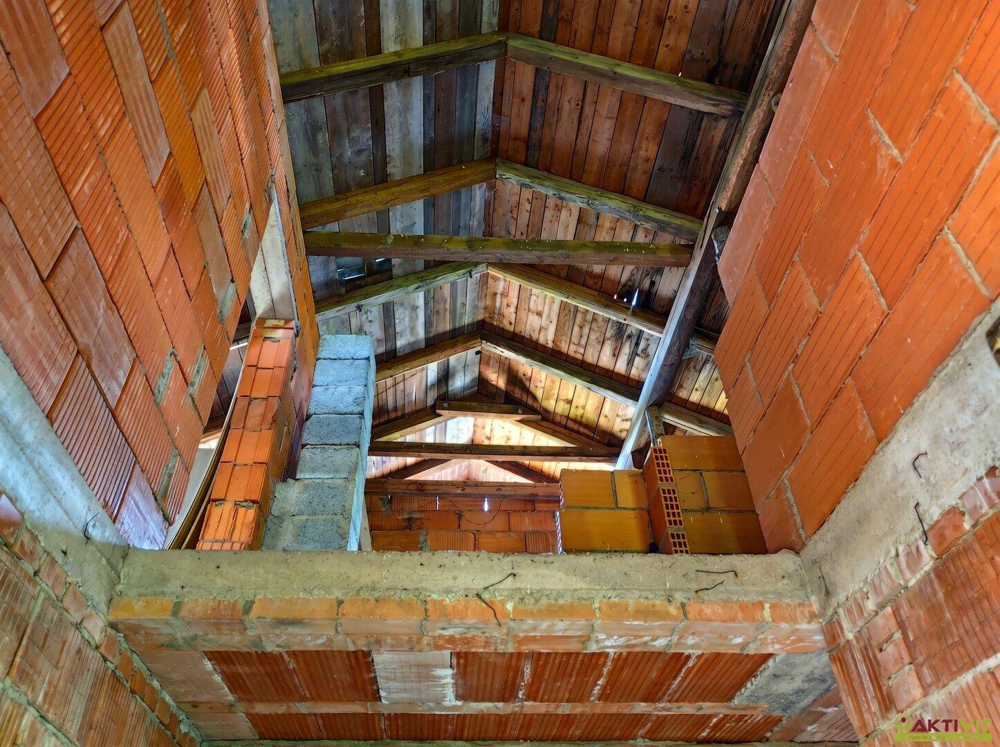 Blick in den unfertigen Dachboden mit sichtbaren Holzbalken und Ziegelwänden im Rohbau.